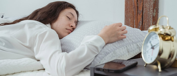 A person sleeping in a comfortable bed with a clock showing the time